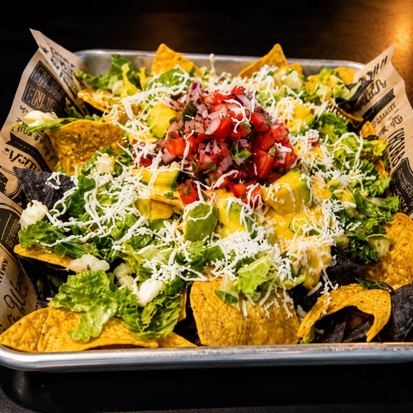 A large tray of nachos with cheese, lettuce, avocado, pico de gallo, and shredded white cheese.