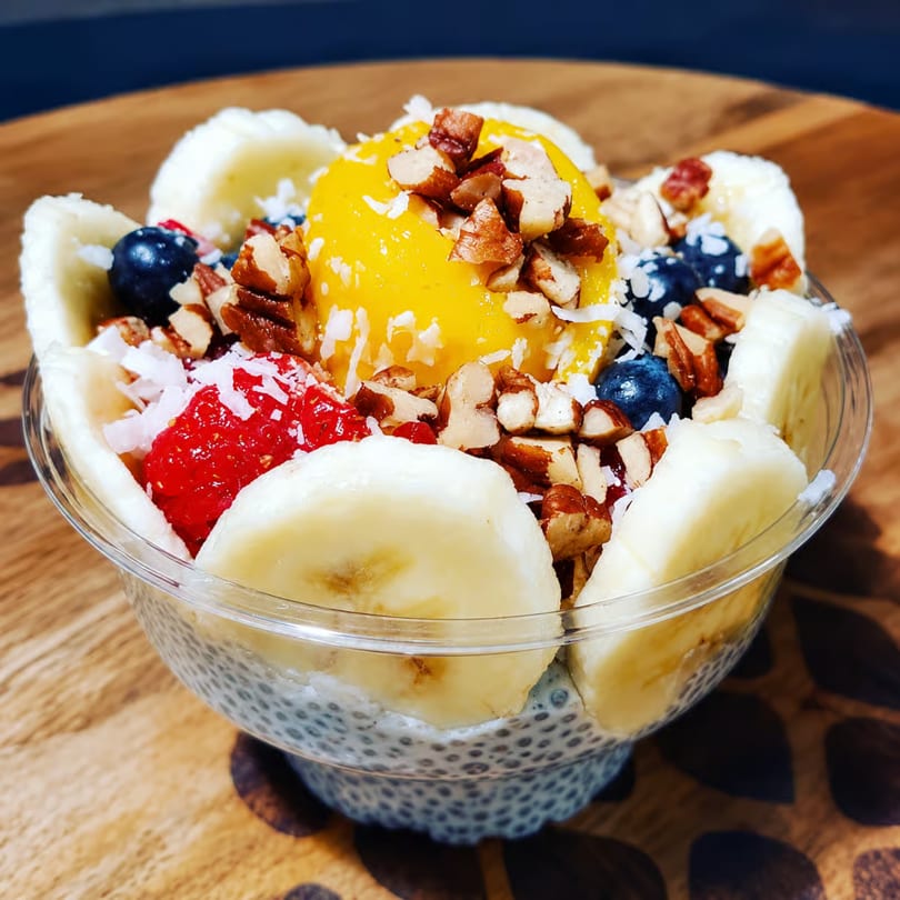 Chia pudding bowl topped with mango, bananas, blueberries, strawberries, pecans, and coconut flakes.
